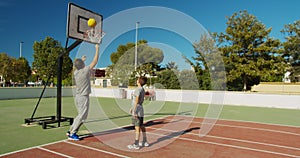 Father with son playing basketball on outdoor court.