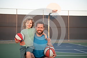 Father and son playing basketball. Portrait of dad embracing little boy who holding basketball ball at playground.