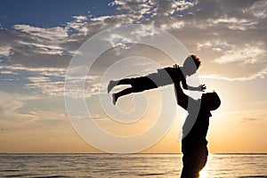 Father and son playing on the beach at the sunset time.