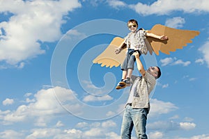 Father and son playing with cardboard toy wings in the park at t