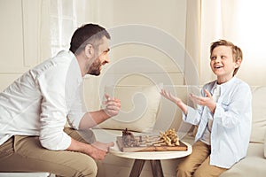 Father and son playing chess and looking at each other at home