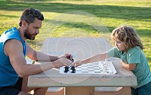 Father and son playing chess spending time together in park. Child playing board game with parent. Men like chess game