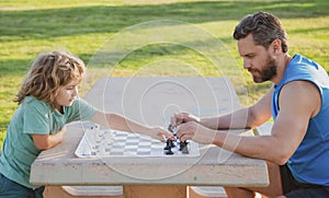 Father and son playing chess spending time together in park. Child playing board game with parent. Men like chess game