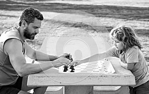 Father and son playing chess spending time together in park. Child playing board game with parent. Men like chess game