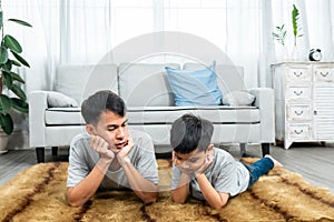 Father-son playing on floor in living room, lying down position raise hands chin rest chin on hands, two people