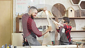 Father and son playing knights with wooden DIY swords at carpenter workshop