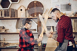 Father and son playing knights with wooden DIY swords at carpenter workshop