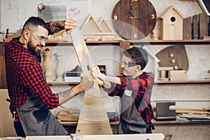 Father and son playing knights with wooden DIY swords at carpenter workshop