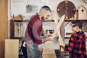 Father and son playing knights with wooden DIY swords at carpenter workshop