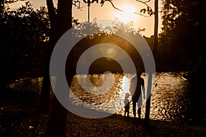 Father and son playing in the park near lake at the sunset time. Concept of family love and of summer vacation silhouette