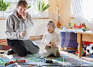 Father and son playing with racing cars on racetrack, indoors, t