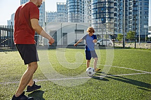 Father and son playing soccer training on football pitch during sunny summer day