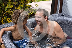 Father and son playing together in a hot tub outdoors. Laughing and having fun in a warm spa in the back yard