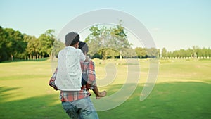 Father and son playing together in park. Man running on green field with boy