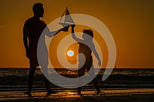 Father and son playing with toy ship on sea. Sunset silhouette of father son dreaming on cruise. Dreaming to travel