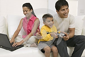 Father and son playing video game, mother using pc