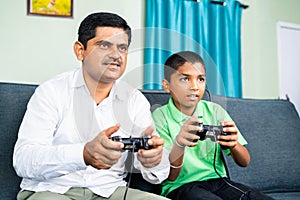 Father and son playing video game using game pad at home during weekend holidays - concept of entertainment, bonding and