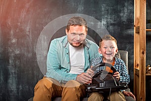 Father and son playing video games on the couch. Happy father and son with wheel console while playing game at home