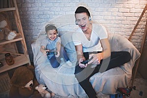 Father and son are playing video games on tv at night at home.