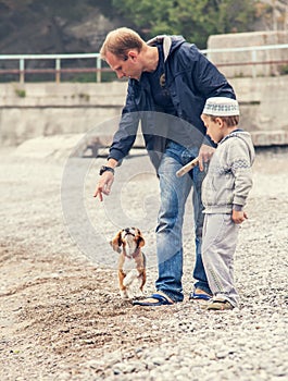 Father and son playing wirh little puppy on the seaside