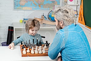 Father and son. Pupil kid thinking about his next move in a game of chess. Dad with his child son are playing Chess