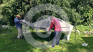 Father and son put tent cloth on garden bower roof construction