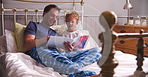 Father And Son Reading Book In Bed Together