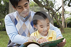 Father And Son Reading Book In Park