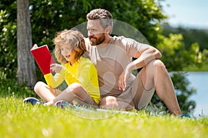 Father and son reading book in park, man encourages boy to knowledge, family education. Father and child read book