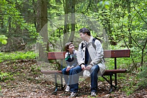 Father and son relaxing on bench after a hike in the woods