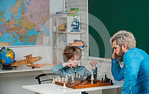 Father and son relaxing together. Nice concentrated little boy sitting at the table and playing chess with his father