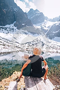 Father and son resting near the mountain lake and enjoying the snow mountains and water surface beauties. Active leisure, spring