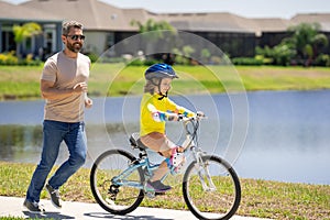 Father and son riding bike on a park. Child in safety helmet with father riding bike on summer day. Father teaching son