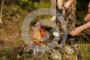 Father and son roasting marshmallow on skewer over the bonfire in forest. The concept of adventure, travel, tourism and camping.