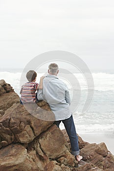 Father And Son On Rocks Looking At Sea View At Beach