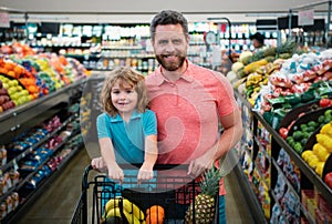 Father and son with shopping basket purchasing food in a grocery store. Customers family buying products at supermarket.