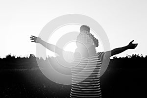 Father and son silhouette walking on the field at the sunset time, boy sitting on mans shoulders. Concept of happy