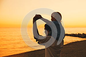 Father and son silhouettes at sunset on a sea beach.