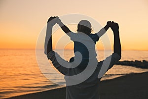 Father and son silhouettes at sunset on a sea beach.