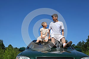 Father and son sit on roof of car in day