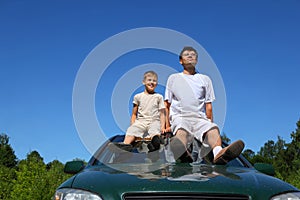Father with son sit on roof of car in day-time