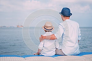 Father and son sit on the sea pier and look on the ship on horizont line