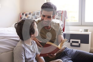 Father And Son Siting On Bedroom Floor Reading Book Together