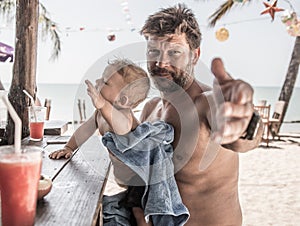 father and son sitting at beach bar counter and require the drinks