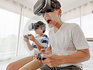 A father and son Sitting in bed. Asian family have fun and enjoy playing the game by wearing virtual glasses. On the bed in the