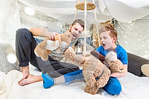 Father and son sitting in blanket fort and playing with teddy bears