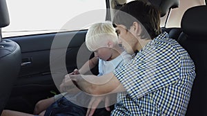 Father with son sitting in car seat and playing on smart phone while having car ride in backseat