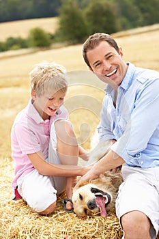 Father And Son Sitting With Dog On Straw Bales In