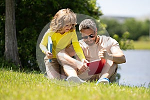 Father and son sitting on green grass in garden and reading book together. Happy family reading book together in green
