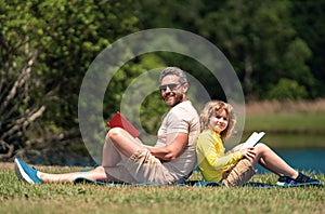 Father and son sitting on green grass in garden and reading book together. Happy family reading book together in green
